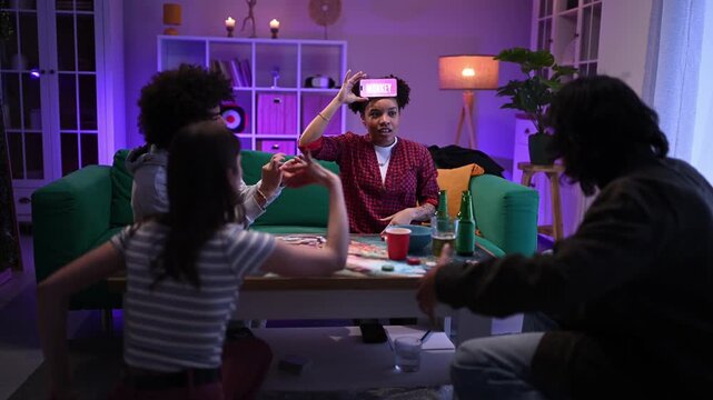 Group of diverse friends playing charades with smartphone at a house party having fun and laughing