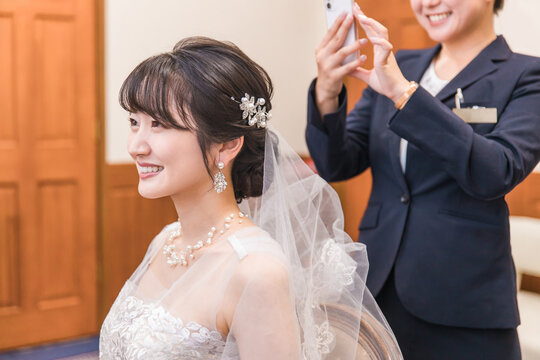 A planner woman taking photos with a smartphone of a bride and groom in a wedding dress preparing for a wedding ceremony and reception