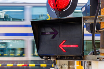 赤く点灯する踏切の方向指示器と通過する電車