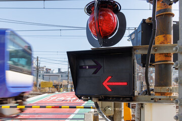 赤く点灯する踏切の方向指示器と通過する電車