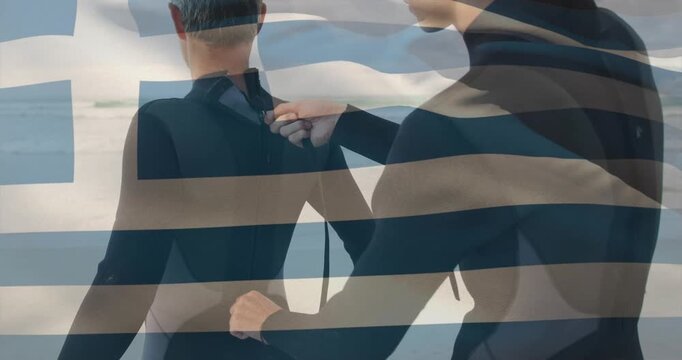 Assistant reaching behind zipping wearer's wetsuit on shore, preparing for surf with flag overlay