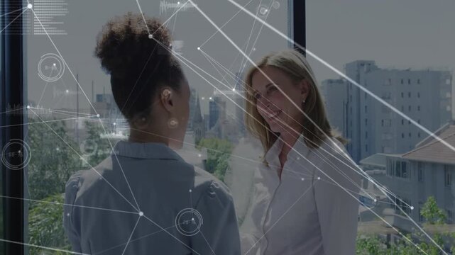 Two women conversing by big window discussing business strategy, sparking HUD overlay mapping data
