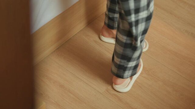 Hotel room doorway empty slippers left on wooden floor as guest steps toward exit view through doorframe, quiet evening mood, solitary departure and subtle movement, clean parquet texture and intimate