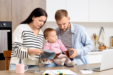 Sad young couple with their baby and empty wallets planning budget in kitchen