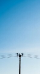 Fototapeta premium Electric power line tower against clear blue sky with sunlight and clouds background