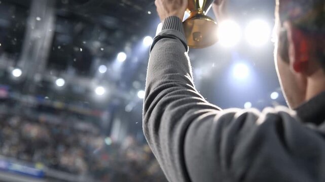 Person lifts a trophy in celebration inside a large sports arena during a championship event