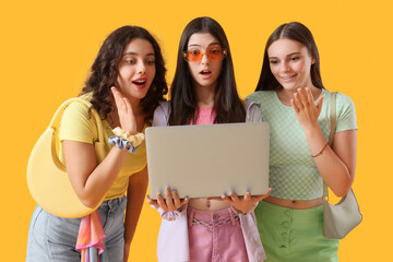 Shocked teenage girls with laptop on yellow background
