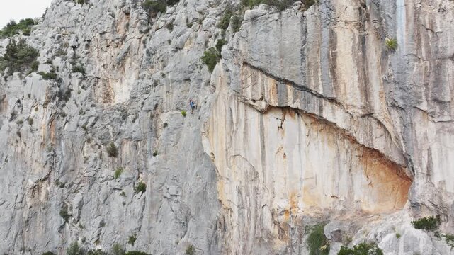AERIAL: Drone shot reveals a young woman lead climbing on a vertical limestone wall. Rugged texture of the Croatian coastline provides a stunning location for adrenaline sport climbing activities.