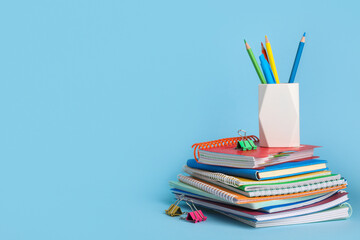Fototapeta premium Stack of different notebooks with pencils holder on blue background