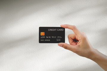 Hand holding a black credit card on white wall background. Conceptual image representing cashless payment, online shopping and modern consumer lifestyle.