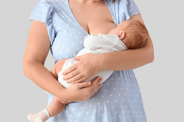 Beautiful young mother breastfeeding her cute little baby on grey background, closeup