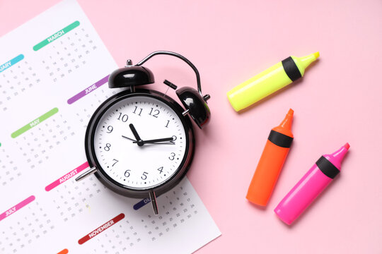 Calendar with alarm clock and markers on pink background