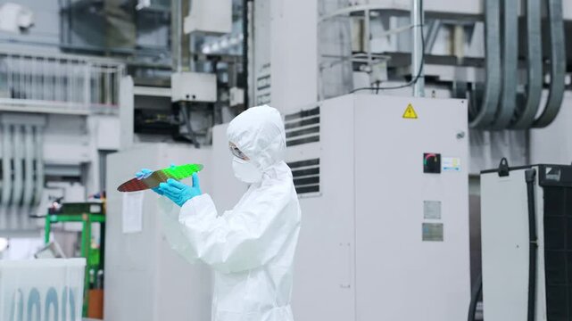半導体工場でシリコンウエハーを検査する防塵服を着た女性作業員