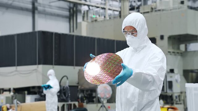 半導体工場でシリコンウエハーを検査する防塵服を着た男性作業員