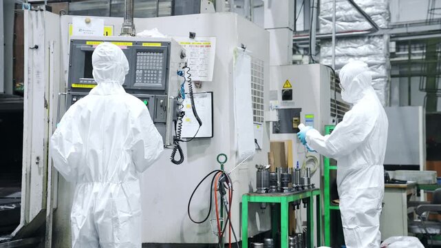 Rear view of male and female workers wearing protective clothing walking in a factory