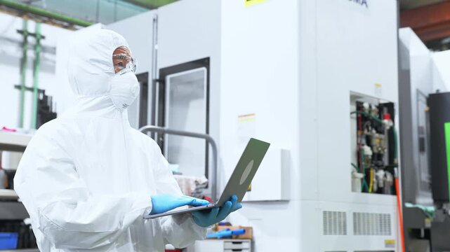 ノートパソコンを持って工場で作業する防護服を着た男性作業員