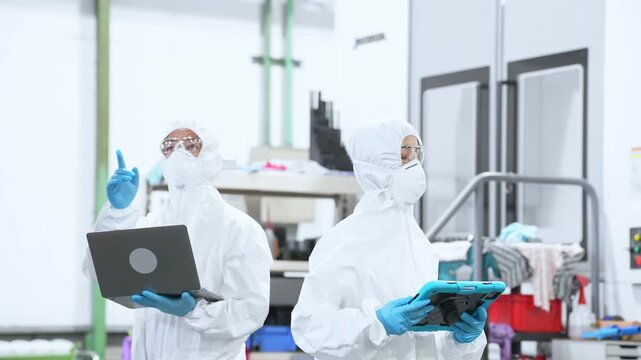デジタルデバイスを持って工場で作業する防護服を着た男女作業員