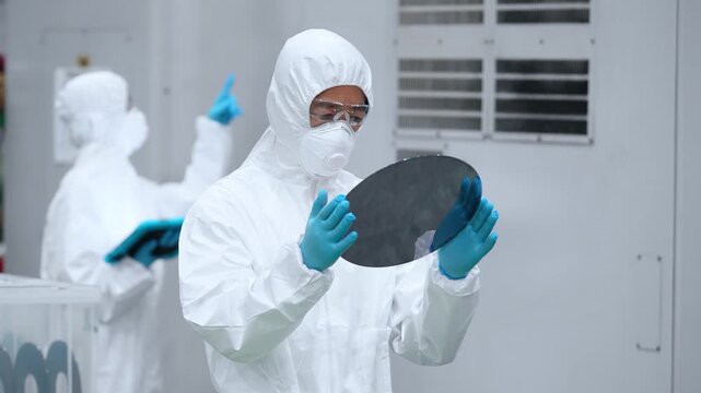 半導体工場でシリコンウエハーを検査する防護服を着た男性作業員