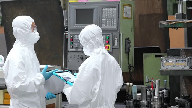 Male and female workers wearing protective clothing operating machines in a factory