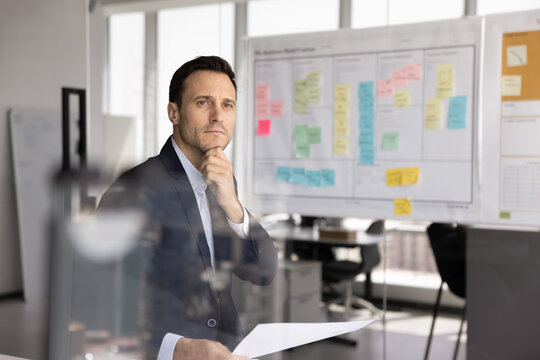 Analytic work. Thoughtful middle adult businessman product owner hold printed finance report in office touch chin look away contemplate strategic decision consider data insights analyze sales progress