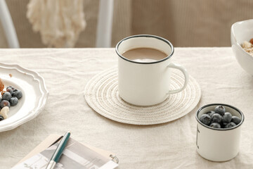 Cup of Coffee with Milk and Fresh Blueberries on a Sunny Breakfast Table, Morning Coffee and Blueberries on Table with Notebook and Teapot in Background