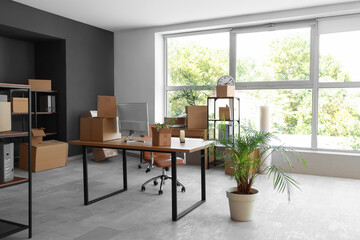 Fototapeta premium Modern workplace with computer monitor and cardboard boxes in office on moving day