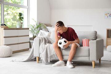 Upset teenage boy with ball watching football game on sofa at home © Pixel-Shot