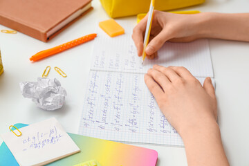 Naklejka premium Woman writing math formulas in copybook and stationery on light table, closeup