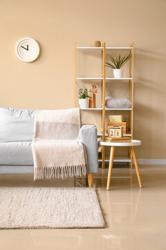 Interior of living room with sofa, wooden rack and table near wall with hanging clock