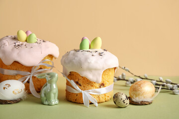Composition with delicious Easter cakes, green porcelain bunny and painted eggs on color background