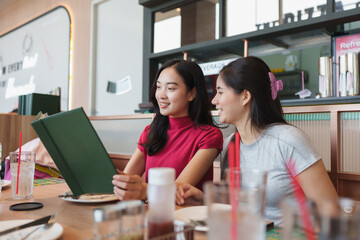Asian friends choosing food from menu in restaurant
