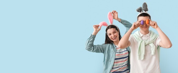Fototapeta premium Funny young couple in bunny ears and with Easter eggs on light blue background with space for text