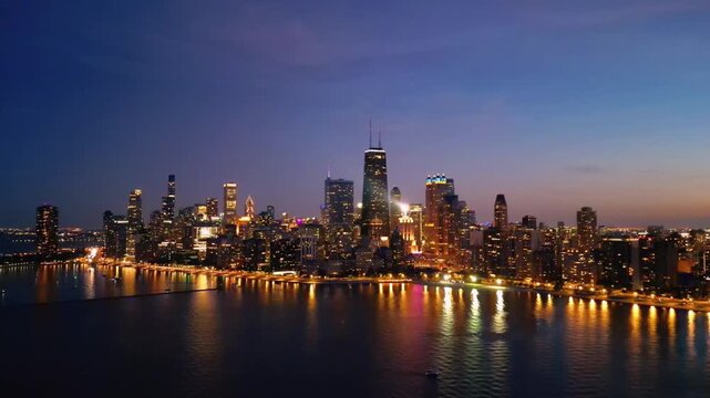 A cinematic drone shot of Chicago from over Lake Michigan at night, where the skyline glows with city lights reflecting across the dark water, creating a bold and dramatic aerial view.