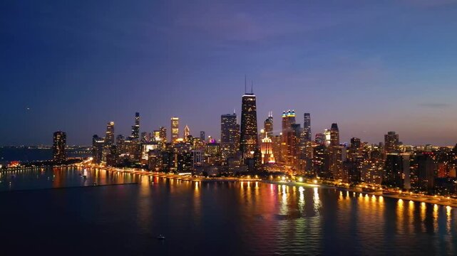A cinematic drone shot of Chicago from over Lake Michigan at night, where the skyline glows with city lights reflecting across the dark water, creating a bold and dramatic aerial view.