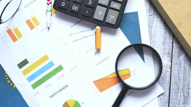 Business and finance concept, magnifying glass on financial accounting documents with calculator and pen on a wooden table, top view