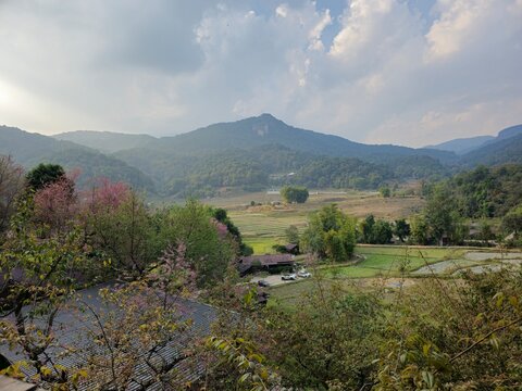 A beautiful mountain landscape with a few houses and a few cars. The sky is cloudy and the sun is shining