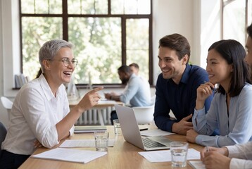 Fototapeta premium Cheerful diverse business team laughing and discussing project on laptop in modern office meeting