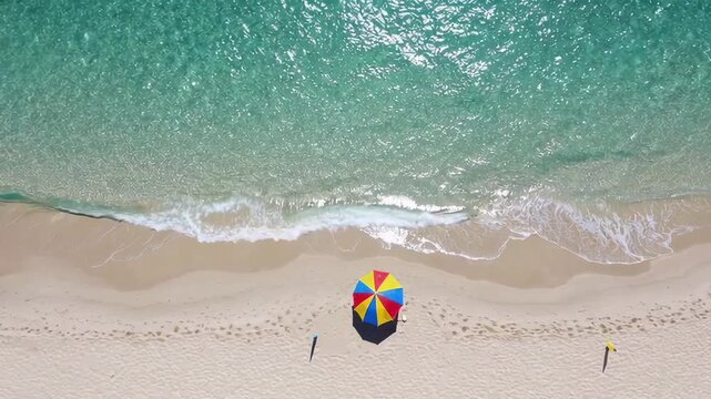 Gentle waves caress the sandy shore where a colorful beach umbrella stands, offering a tranquil and relaxing scene of coastal paradise in slow motion