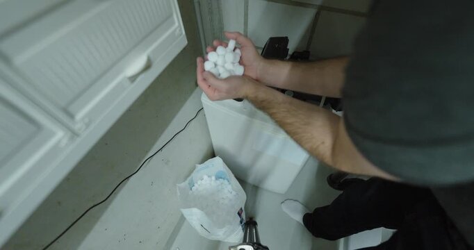 Top view close-up of a person pouring salt into a domestic water softener unit, illustrating home maintenance, limescale prevention and household plumbing care.
