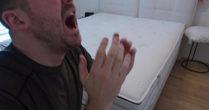 Man sitting next to a mattress sneezing and showing allergic reaction symptoms, illustrating dust mite allergy, bedroom hygiene issues and respiratory health problems.