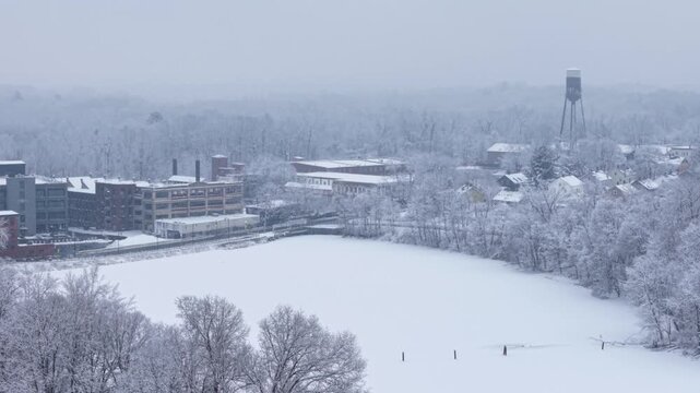 Snow Falling Over Lower Mill Pond's Frozen Surface, Surrounded By Ice-coated Trees And Buildings In Easthampton, MA. aerial sideways shot