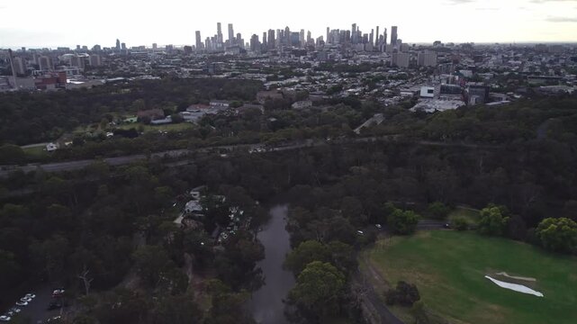 Reverse drone view at sunset day at Studley Park of the Yarra River in the foreground and the Mebourne city skyline in the distance, Victoria, Australia. December 2025