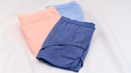 Three folded pairs of colorful underwear in peach, light blue, and navy blue on white fabric background.