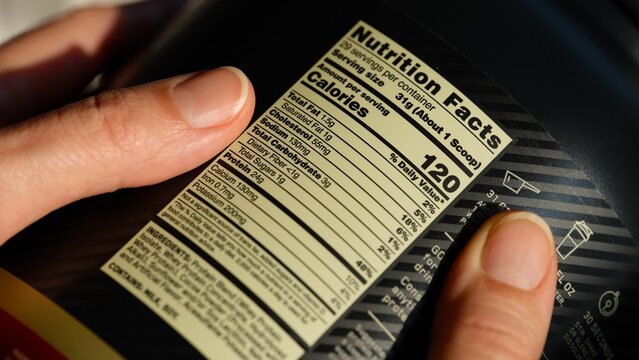 Close-up of black jar of whey protein powder with nutrition facts label in woman hands