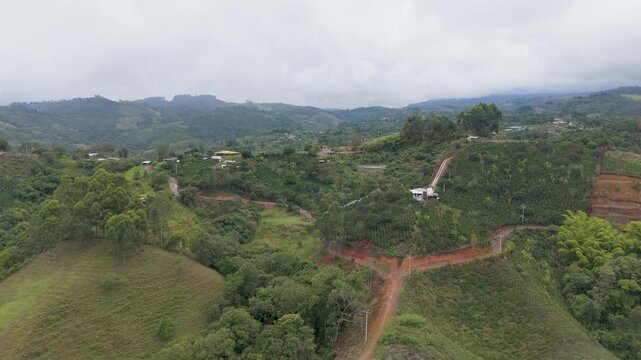 Aerial view of green hills in Popay&aacute;n, featuring small houses and cloudy weather. The landscape shows various shades of green and red soil.