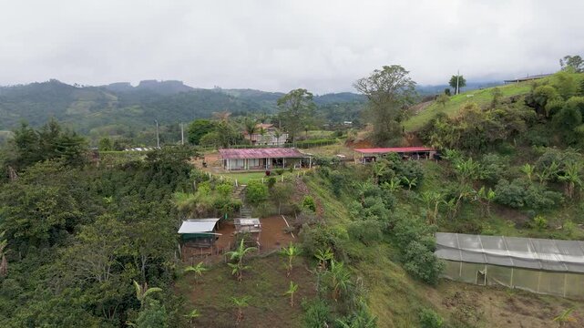 This aerial shot captures a green hilly landscape featuring several buildings and clear paths under a cloudy sky.