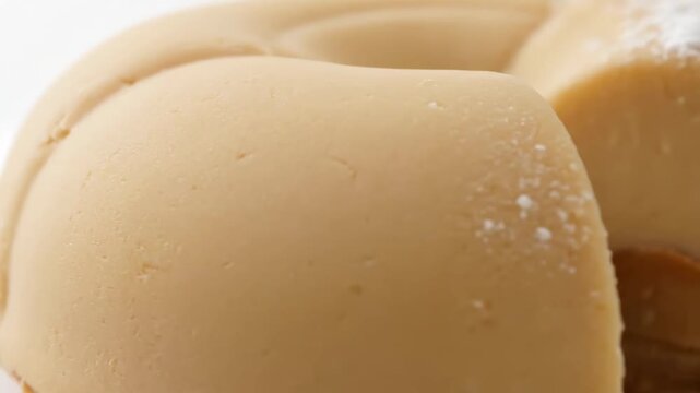 Extreme Macro Close-Up of a Smooth, Creamy Molded Dessert Surface, resembling Flan or Caramel Pudding, highlighting the soft texture against a bright white background.