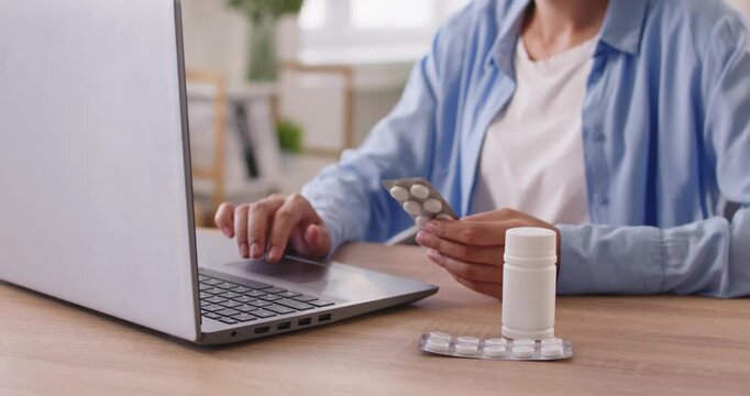 Online pharmacy research by woman with laptop at home. Lady holding pills blister in hand, reading dosage and safety usage guide, drug side effects and article on contraindications for tablets