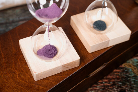 glass hourglass with magnetic sand on wooden stand, books, vintage mood, pocket watch, lifestyle or time management concept
