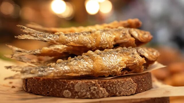 Close-up of Crispy Deep-Fried Smelt (or Sprat) Served on Rustic Rye Bread. Golden whole fish snack on dark toast with warm restaurant bokeh.